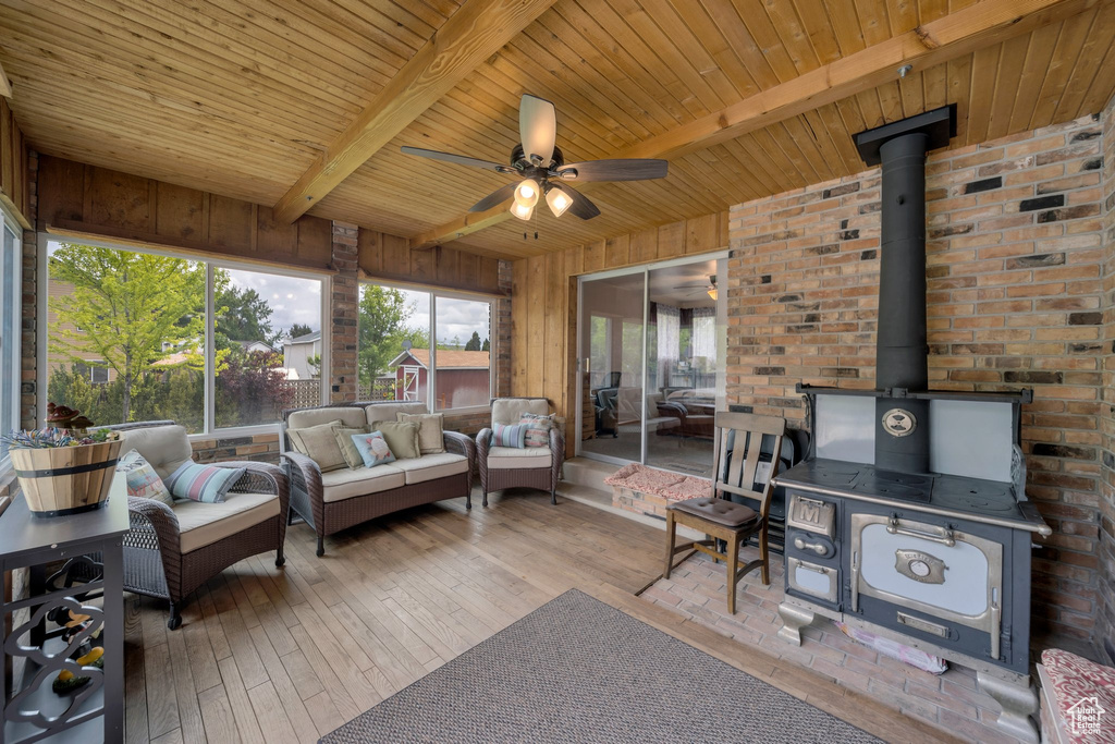Living area featuring a wood stove, beam ceiling, a ceiling fan, wood ceiling, and hardwood / wood-style flooring