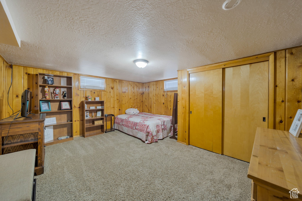 Bedroom with a textured ceiling, carpet, wood walls, a closet, and multiple windows