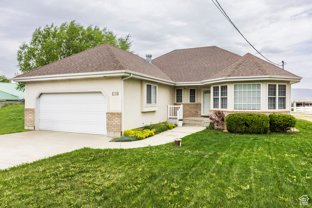 View of front of house featuring brick siding, a garage, a front lawn, driveway, and a shingled roof