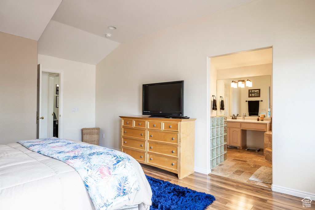 Bedroom featuring light wood-style floors, lofted ceiling, a chandelier, ensuite bathroom, and baseboards