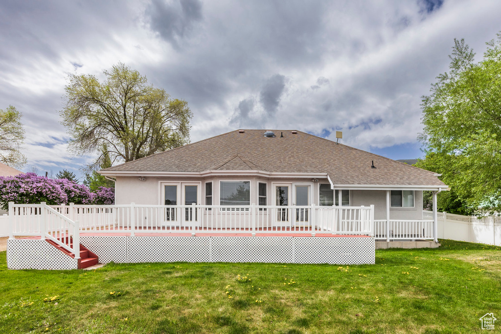 Rear view of house with roof with shingles, a deck, a lawn, and stucco siding