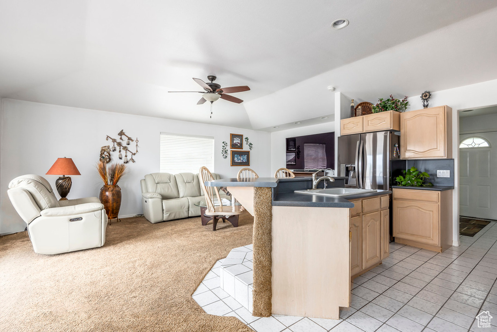Kitchen with open floor plan, light brown cabinetry, ceiling fan, dark countertops, and a sink