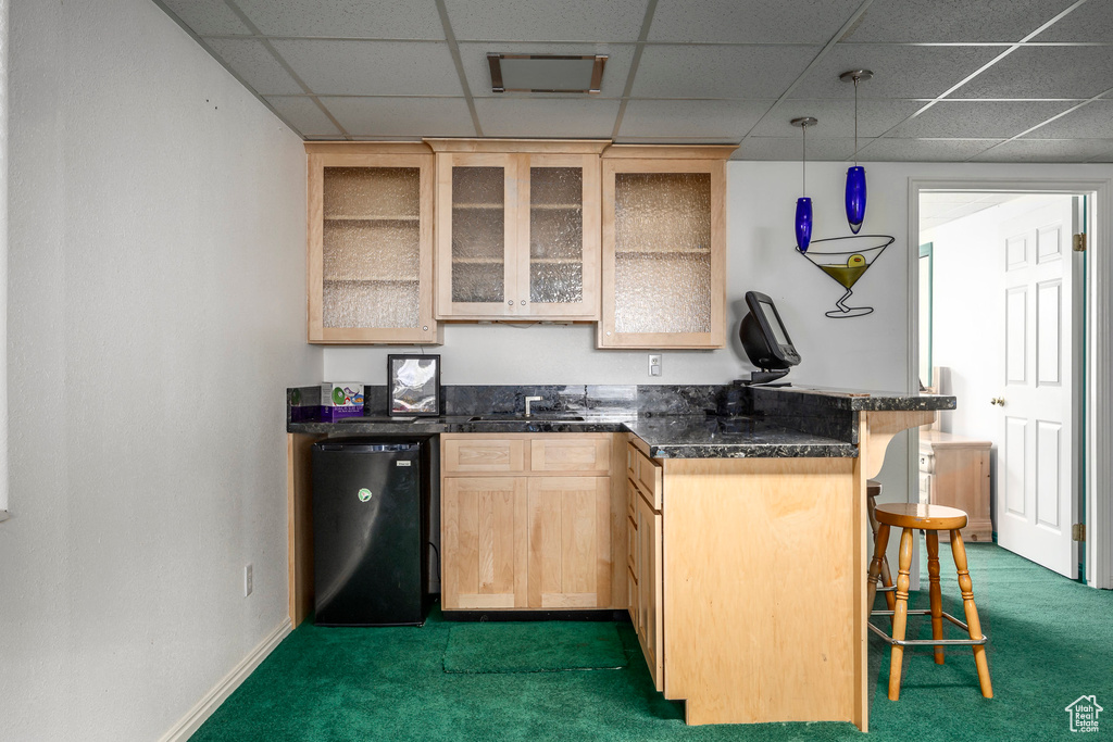 Kitchen featuring light brown cabinetry, dark carpet, a kitchen bar, a drop ceiling, and dishwashing machine
