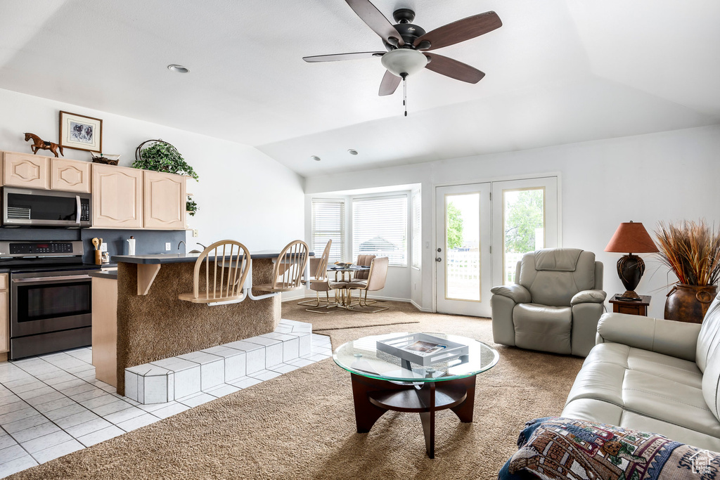 Living room featuring vaulted ceiling, ceiling fan, light colored carpet, and light tile patterned flooring
