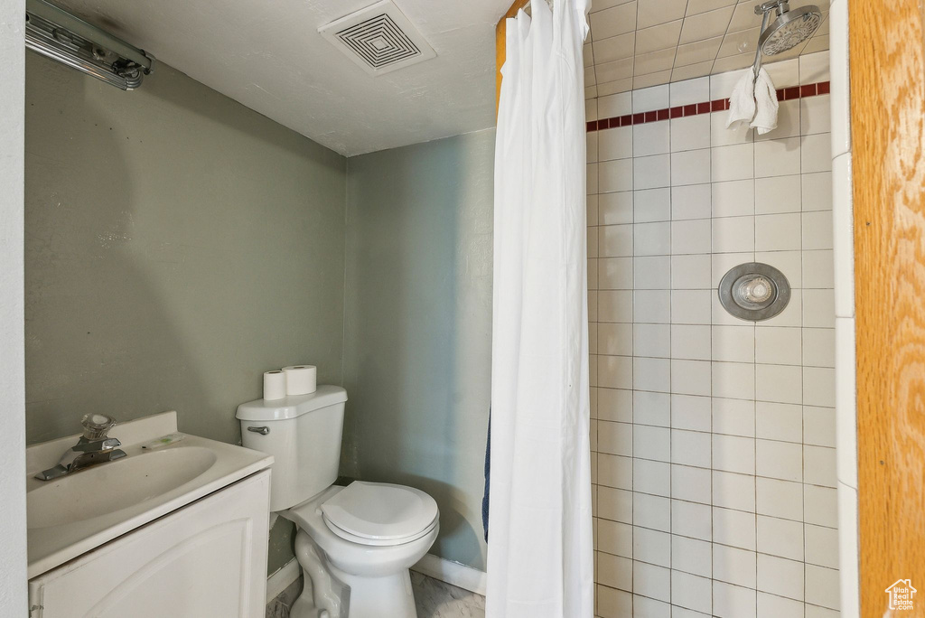 Bathroom featuring toilet, tiled shower, vanity, and baseboards