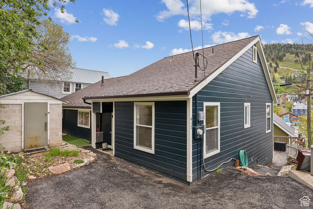 Rear view of property featuring a shed, roof with shingles, an outbuilding, and central AC