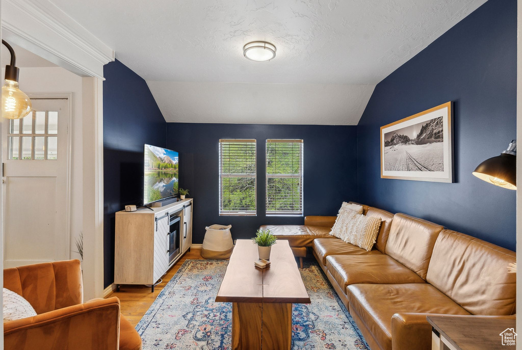 Living room featuring vaulted ceiling, light wood-style flooring, baseboards, and a textured ceiling