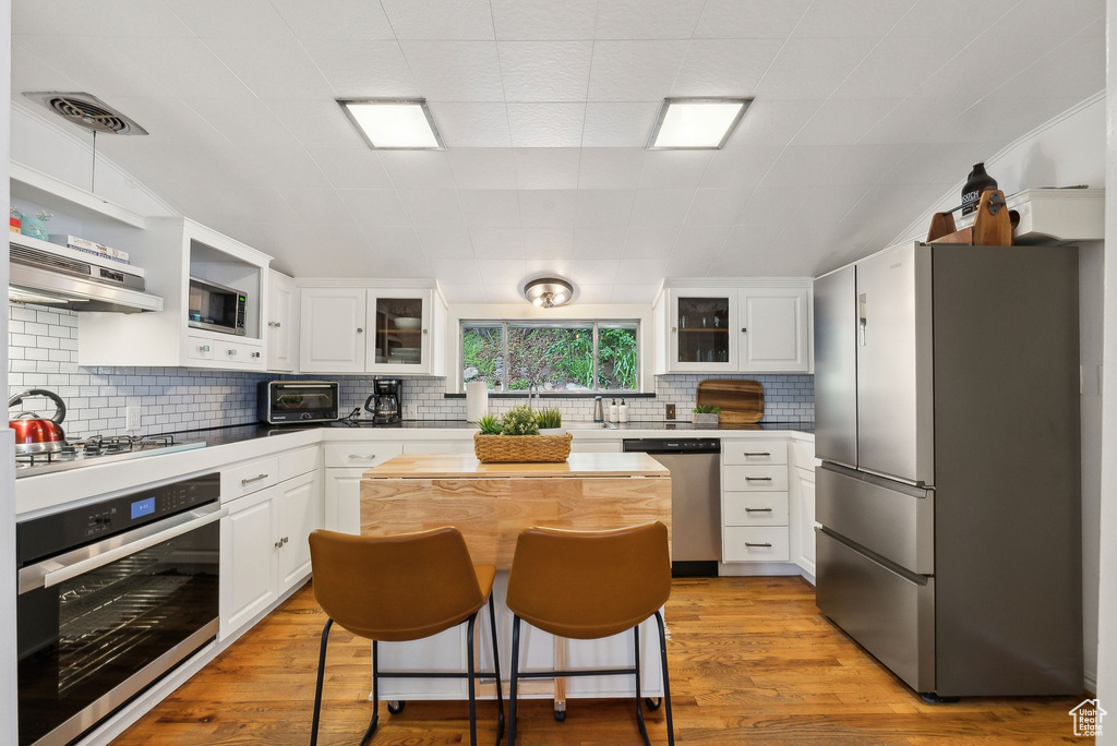 Kitchen with appliances with stainless steel finishes, under cabinet range hood, backsplash, and white cabinetry