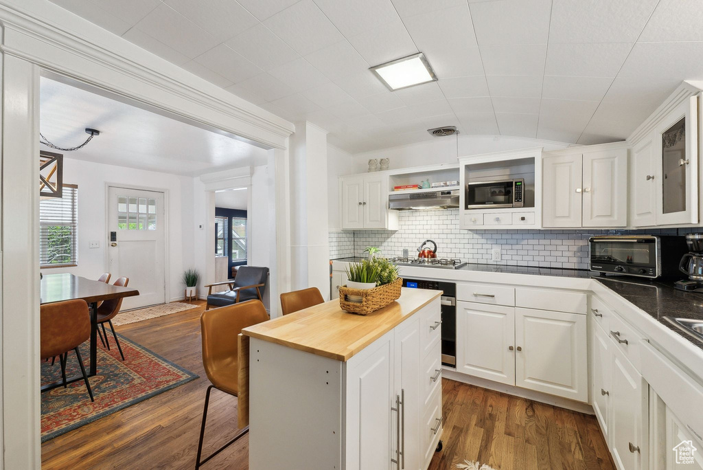 Kitchen with appliances with stainless steel finishes, wood counters, dark wood-style floors, white cabinetry, and vaulted ceiling