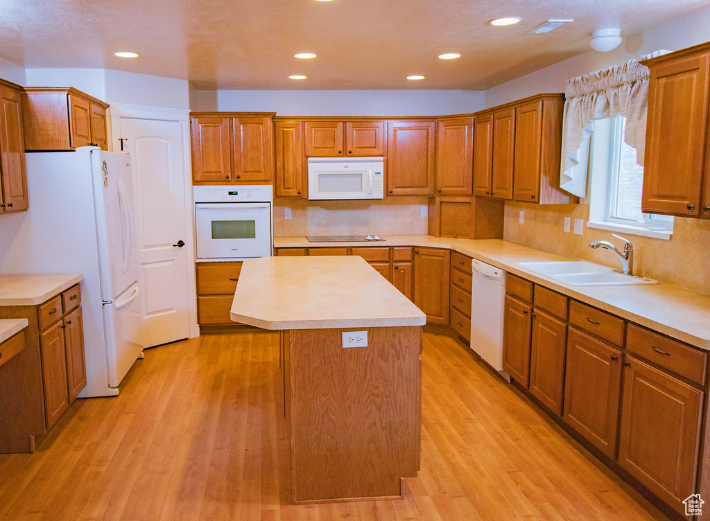 Kitchen with white appliances, a sink, a center island, light wood-style floors, and light countertops
