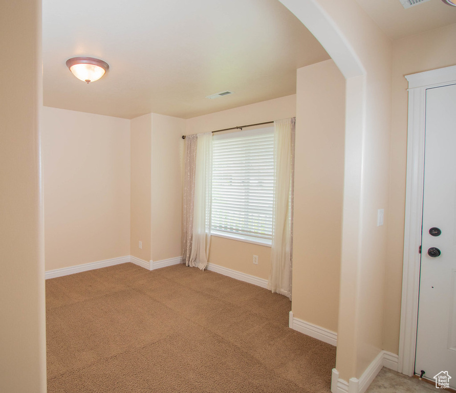 Spare room featuring arched walkways, light colored carpet, and baseboards