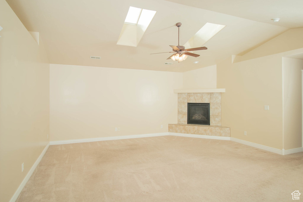 Unfurnished living room featuring a skylight, light colored carpet, lofted ceiling, a fireplace, and baseboards