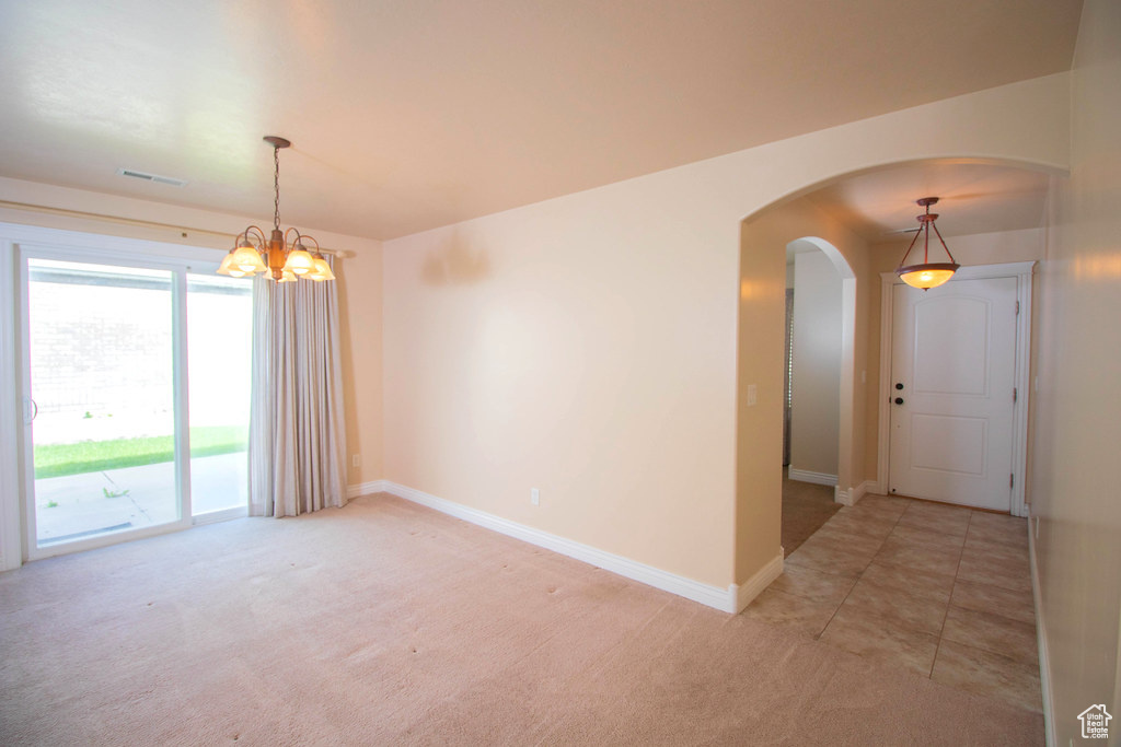 Empty room featuring arched walkways, a chandelier, light colored carpet, and baseboards