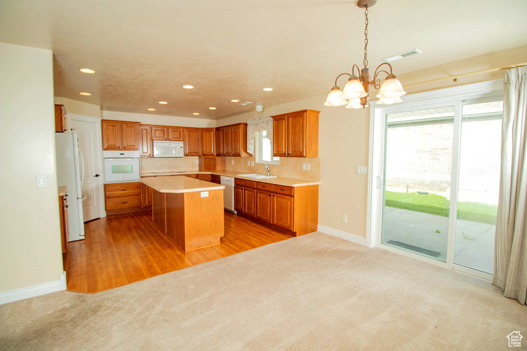 Kitchen featuring white appliances, a sink, light colored carpet, brown cabinetry, and recessed lighting