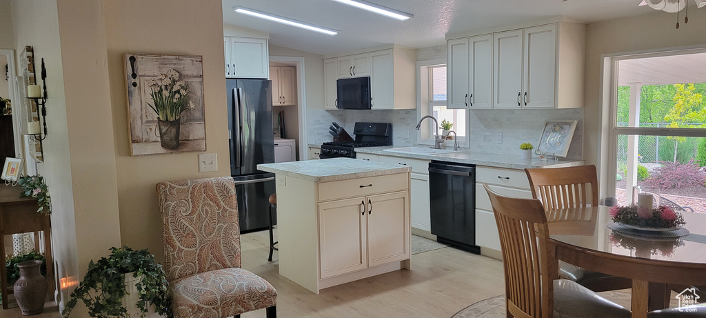 Kitchen with black appliances, a sink, decorative backsplash, light countertops, and light wood-style floors