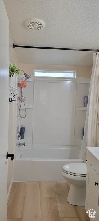 Full bath featuring toilet, shower / tub combo with curtain, vanity, wood finished floors, and a textured ceiling