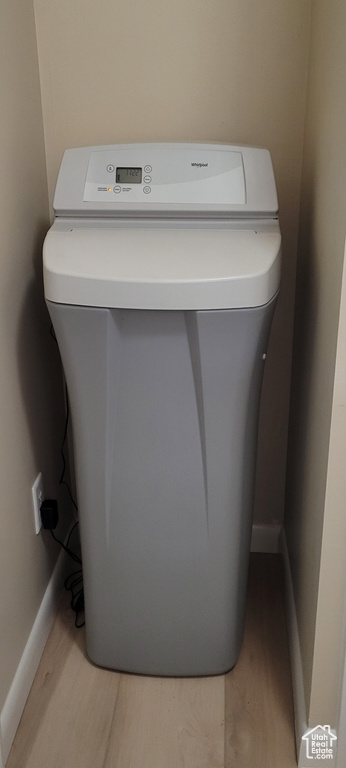 Laundry view of a water softener system, wood finished floors, and baseboards