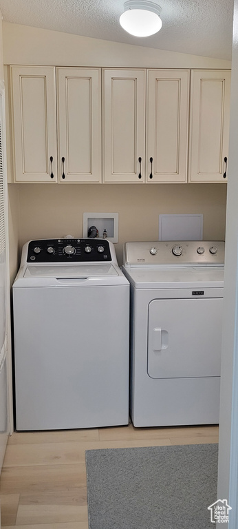 Washroom featuring separate washer and dryer, cabinet space, light wood-type flooring, and a textured ceiling