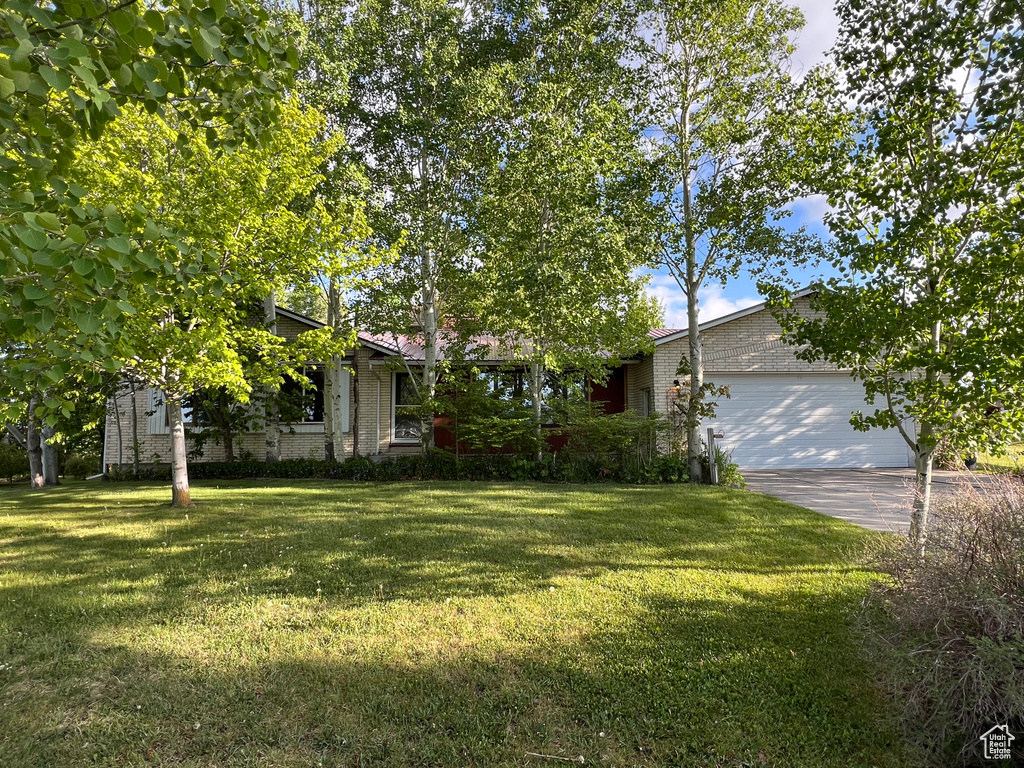 View of front of property featuring an attached garage, a front yard, driveway, and brick siding