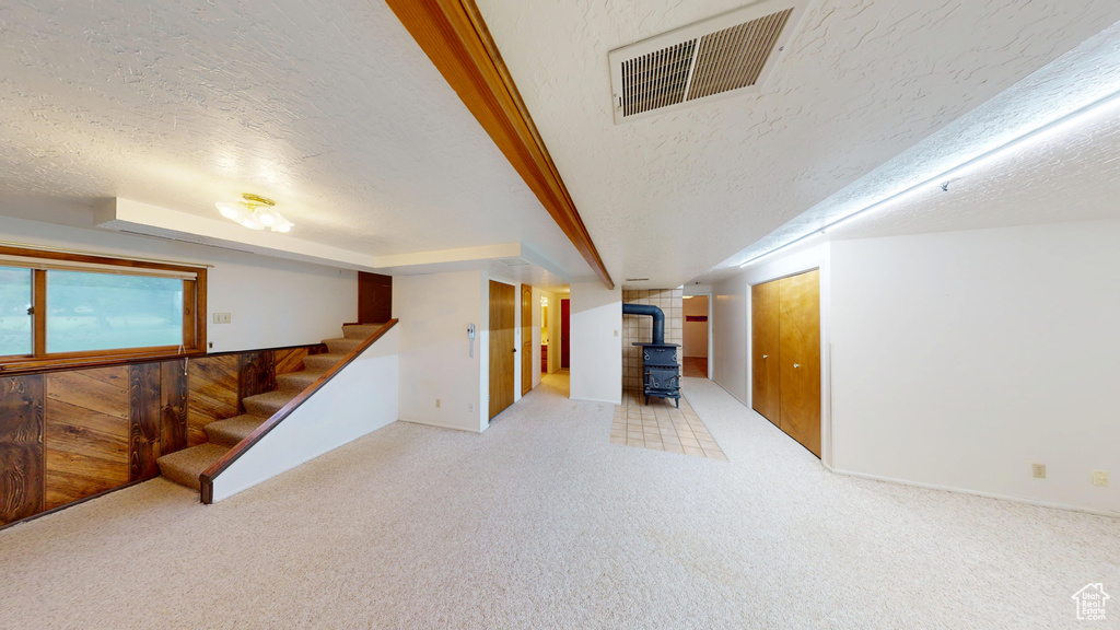 Basement featuring a wood stove, a textured ceiling, stairs, carpet floors, and baseboards
