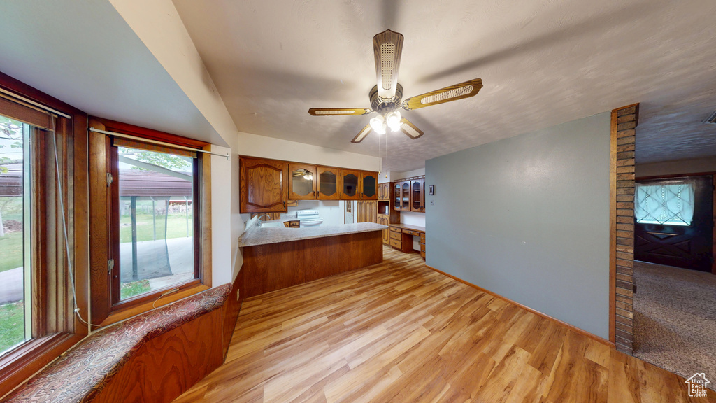 Kitchen with brown cabinets, glass insert cabinets, light wood-type flooring, and healthy amount of natural light