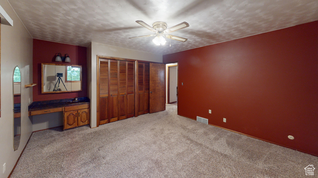 Unfurnished bedroom featuring light carpet, multiple closets, ceiling fan, and a textured ceiling