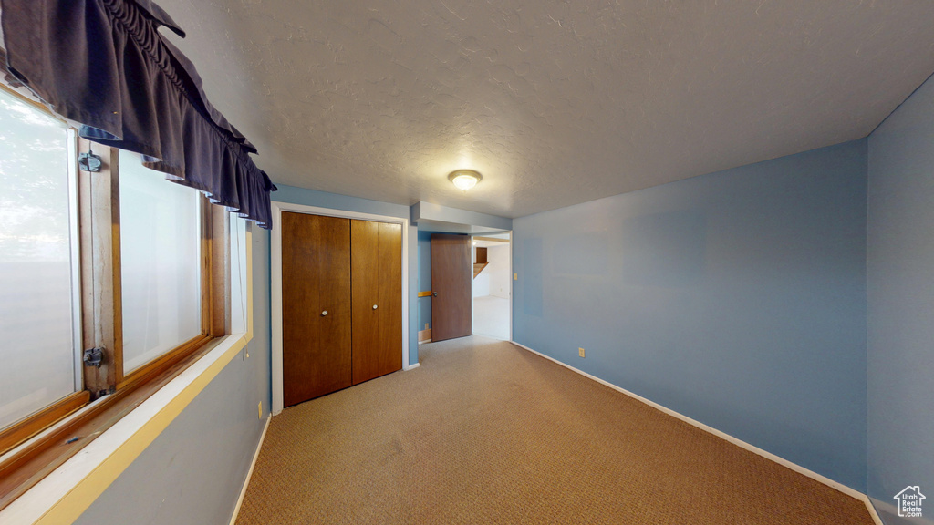 Unfurnished bedroom with light carpet, a closet, baseboards, and a textured ceiling