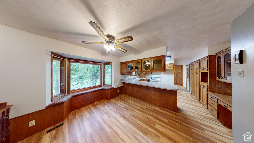 Kitchen featuring a peninsula, brown cabinets, glass insert cabinets, light wood-style flooring, and ceiling fan