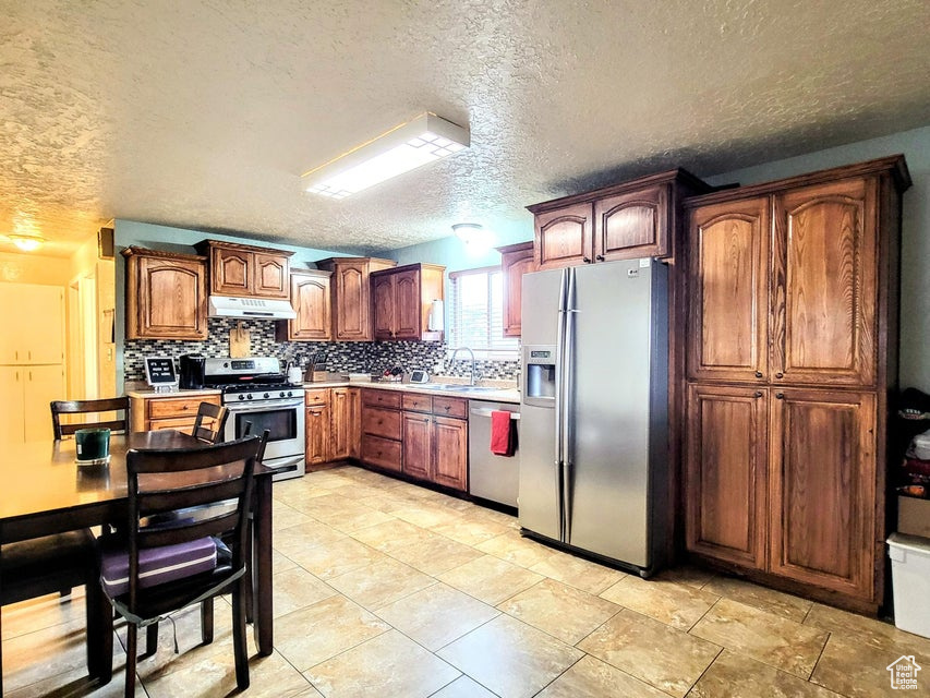 Kitchen with stainless steel appliances, under cabinet range hood, decorative backsplash, light countertops, and a textured ceiling