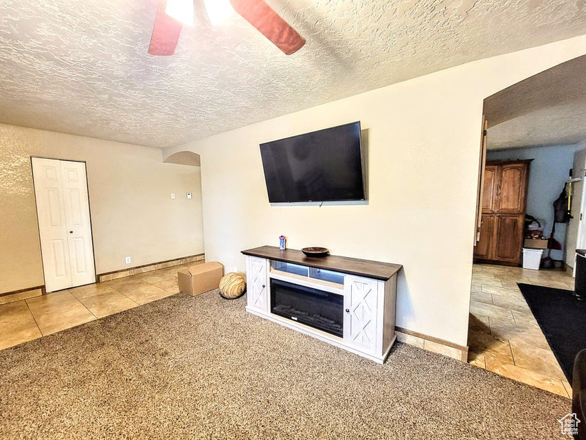 Living area featuring arched walkways, carpet, ceiling fan, a textured ceiling, and baseboards