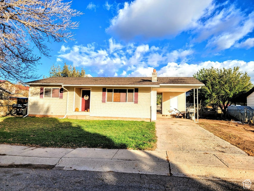 Ranch-style home with a front yard, driveway, a chimney, and a carport