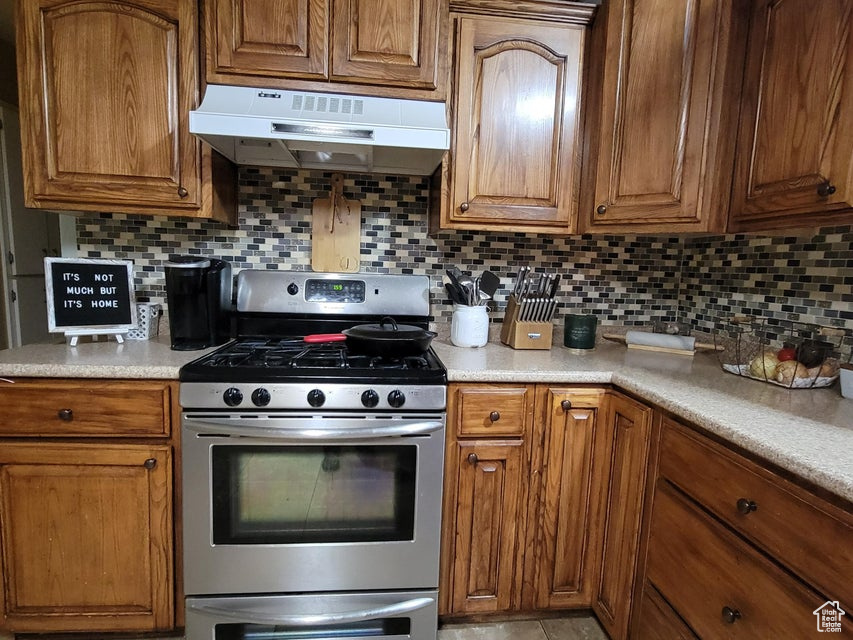 Kitchen with stainless steel gas range, under cabinet range hood, tasteful backsplash, and brown cabinets