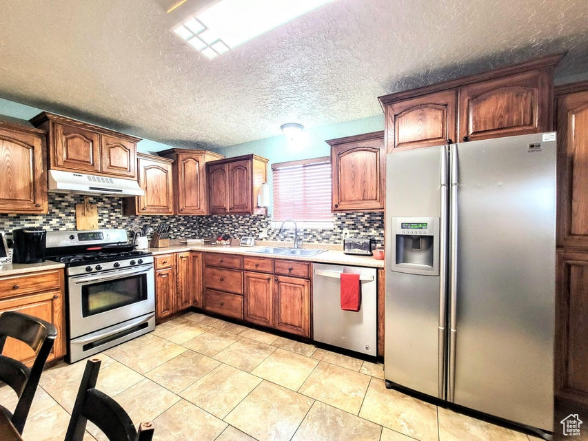 Kitchen featuring appliances with stainless steel finishes, under cabinet range hood, a sink, light countertops, and decorative backsplash