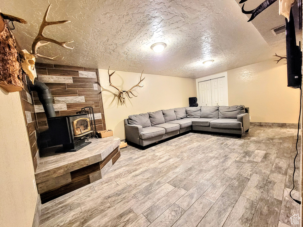 Living room with a wood stove, wood finished floors, a textured ceiling, baseboards, and wood walls
