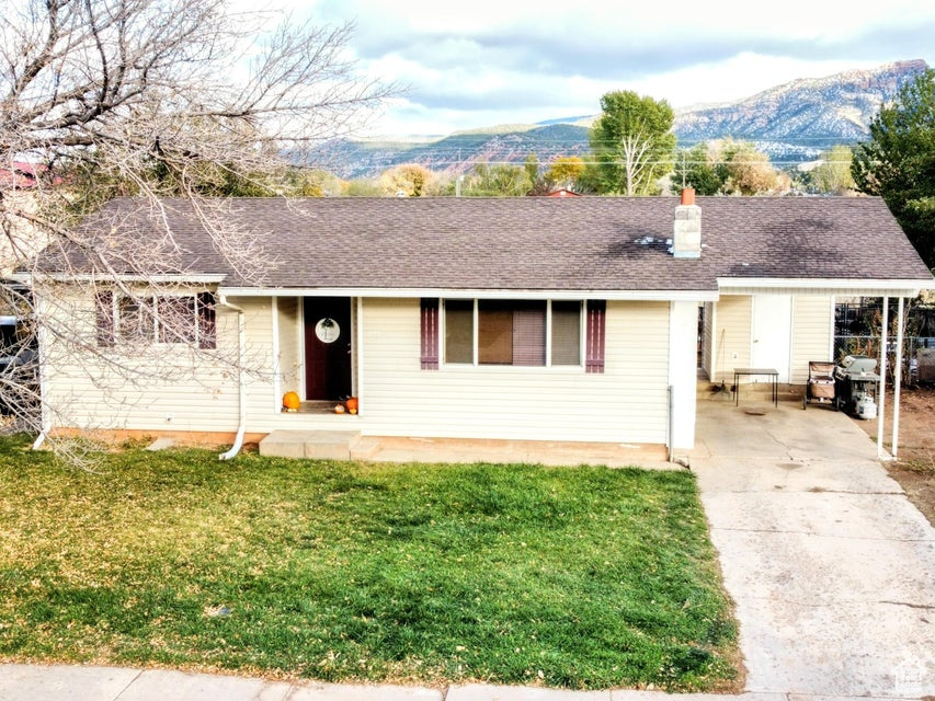 Ranch-style home featuring concrete driveway, a front yard, a chimney, and a mountain view