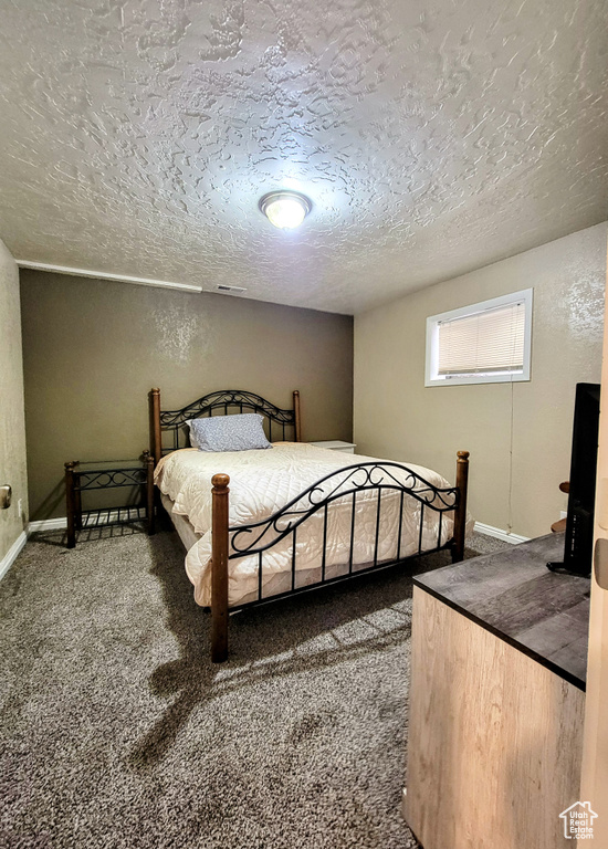 Bedroom with a textured ceiling, carpet, baseboards, and a textured wall
