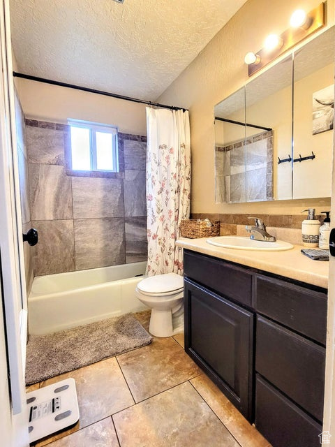 Bathroom with shower / bathtub combination with curtain, tile patterned flooring, vanity, toilet, and a textured ceiling