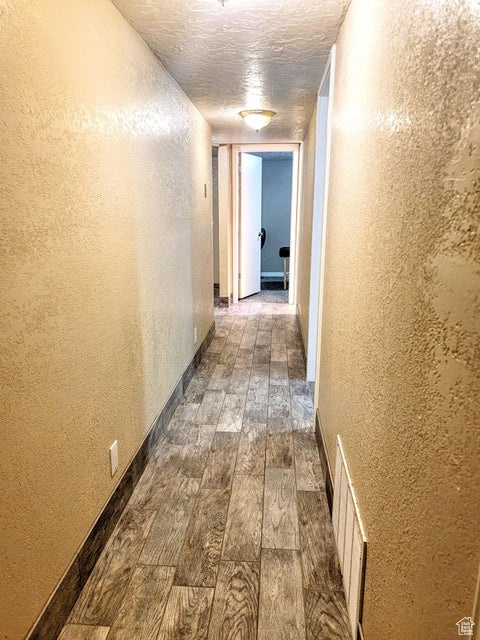 Corridor with dark wood finished floors, a textured wall, baseboards, and a textured ceiling