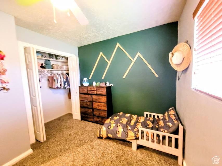 Carpeted bedroom with a textured ceiling, ceiling fan, and a closet