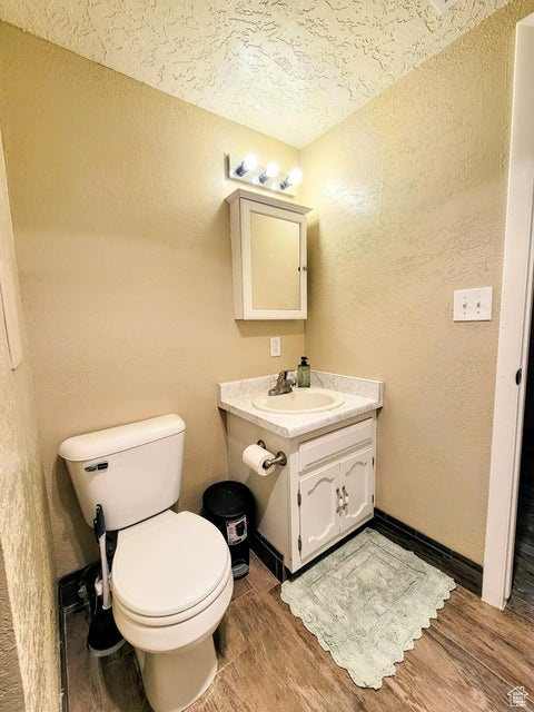 Bathroom with a textured ceiling, toilet, vanity, wood finished floors, and a textured wall