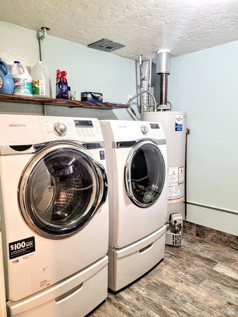 Clothes washing area with light wood-style flooring, water heater, washing machine and dryer, a textured ceiling, and baseboards