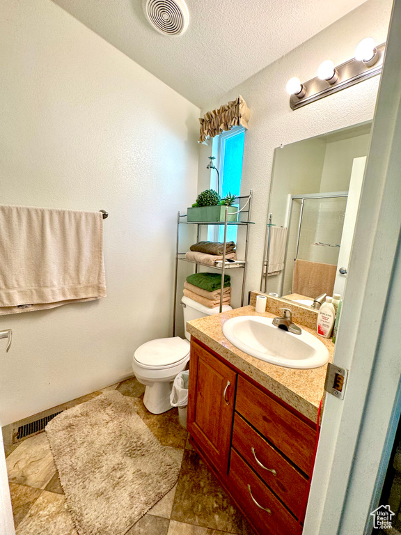Bathroom featuring vanity, toilet, a textured ceiling, visible vents, and a stall shower