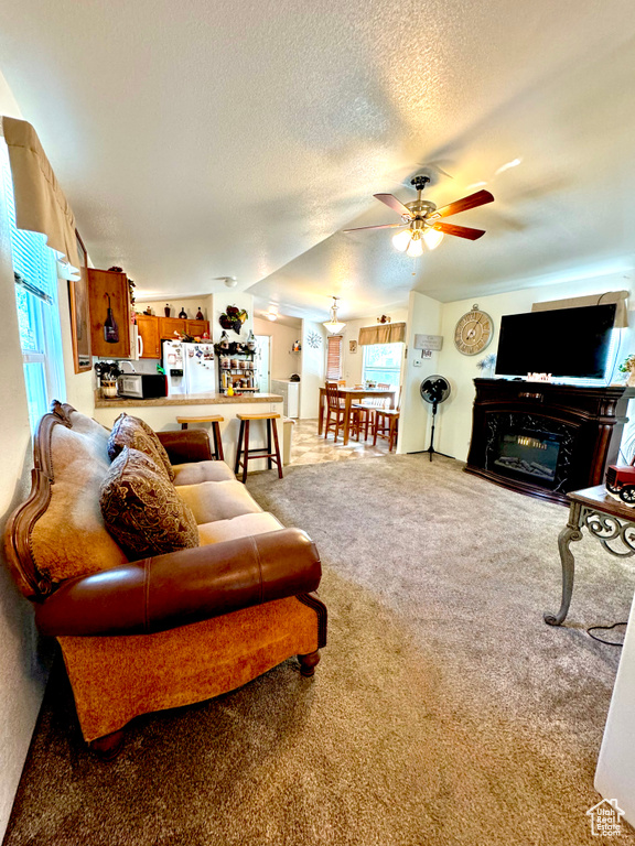 Living room with a textured ceiling, ceiling fan, a glass covered fireplace, and carpet