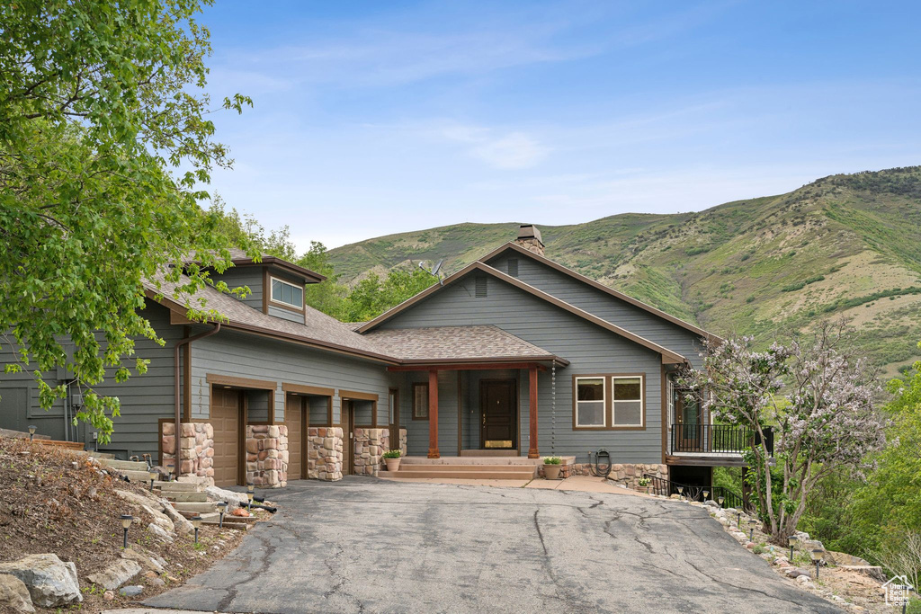 View of front of home with driveway, a mountain view, an attached garage, a porch, and stone siding