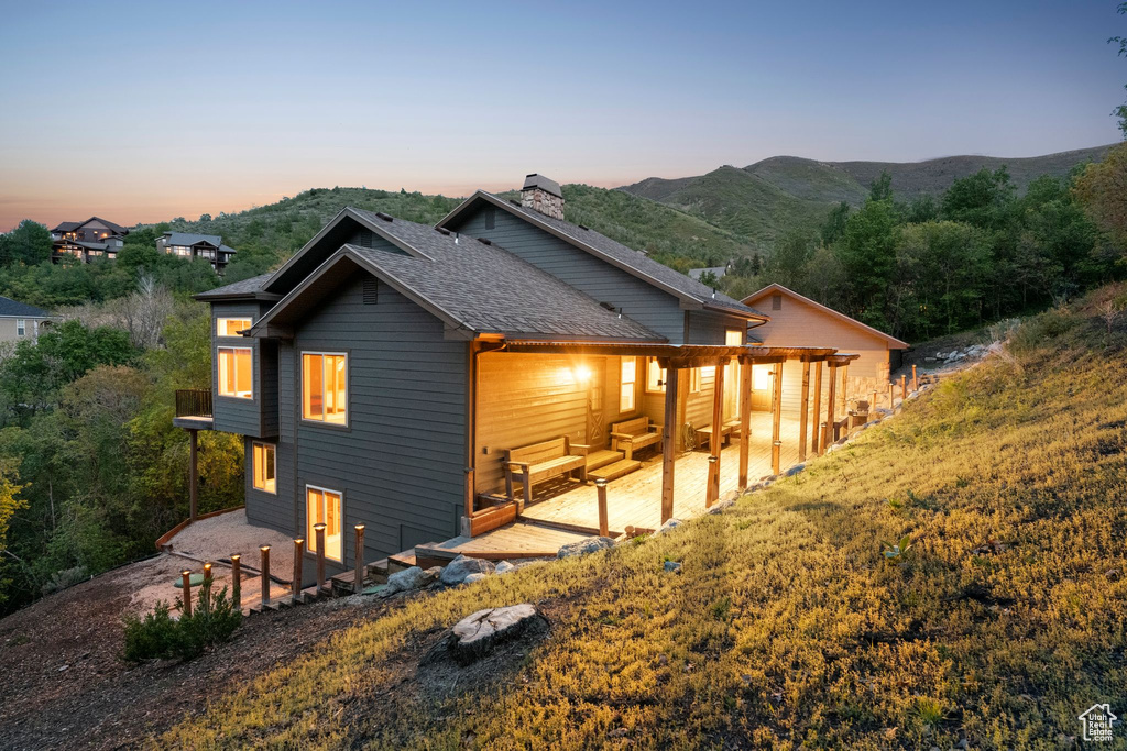 Back of house at dusk with a patio, a chimney, roof with shingles, and a mountain view