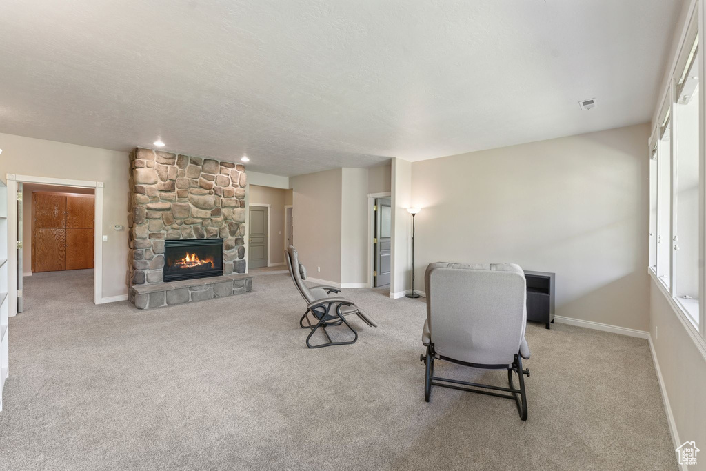 Living area featuring a stone fireplace, light colored carpet, baseboards, and a textured ceiling