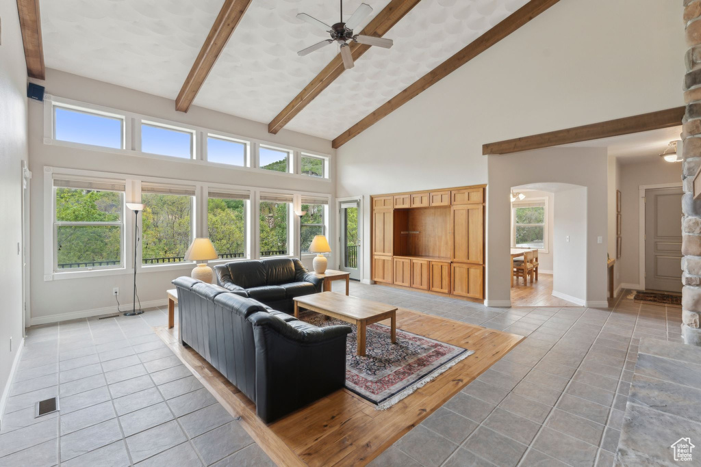 Living area featuring arched walkways, light tile patterned floors, high vaulted ceiling, beamed ceiling, and a ceiling fan