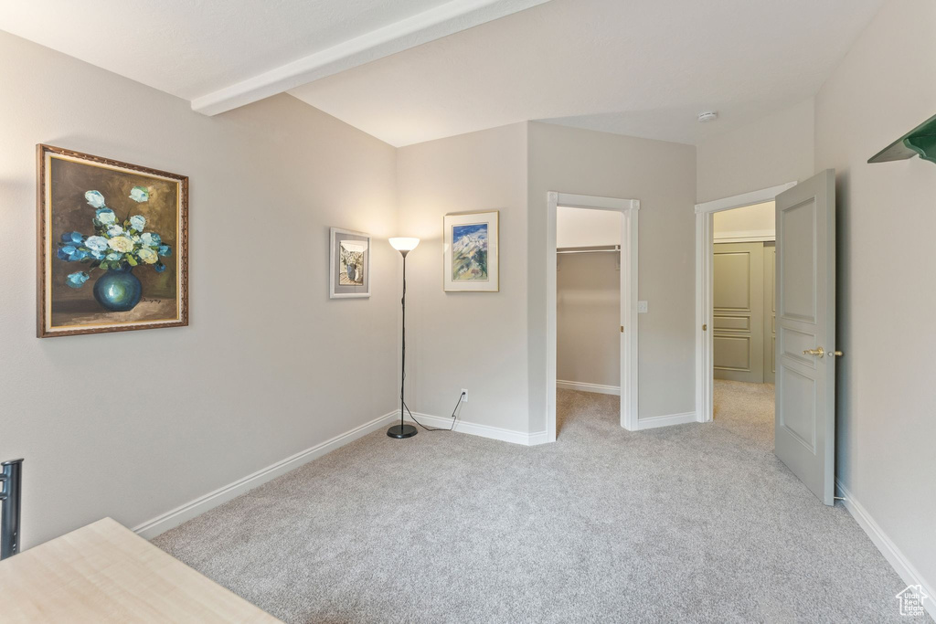 Unfurnished bedroom featuring light colored carpet, baseboards, a walk in closet, and beamed ceiling