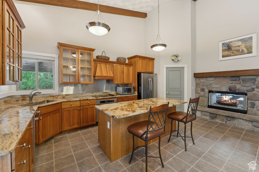 Kitchen with stainless steel appliances, a high ceiling, a sink, dark tile patterned floors, and brown cabinetry