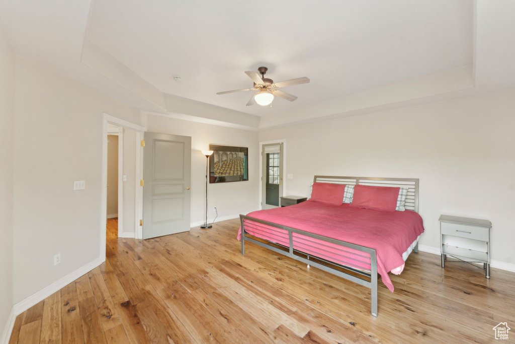 Bedroom with light wood finished floors, a raised ceiling, baseboards, and a ceiling fan
